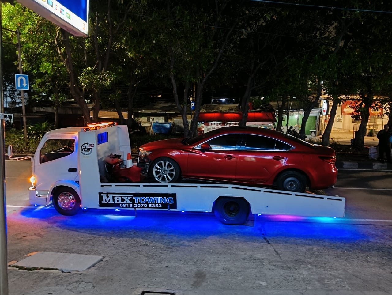 Truk Max Towing mengangkut mobil sedan pada malam hari